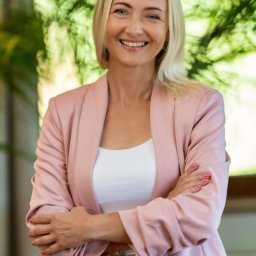 BABCZYŃSKI IT Piotr Babczyński - Portret uśmiechniętej blondynki w różowym żakiecie, skrzyżowane ręce, egzotyczny pasek, zielone tło z liści