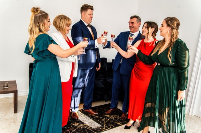 Grupa elegancko ubranych osób w Szczecinie wznosi toast szampanem, na marmurowej podłodze widoczne odbicie światła.