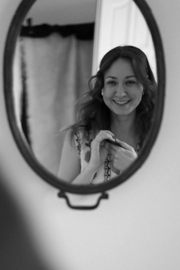 Portret uśmiechniętej kobiety w lustrze w Warszawie, poprawiającej włosy, z widocznym odbiciem wnętrza pokoju.