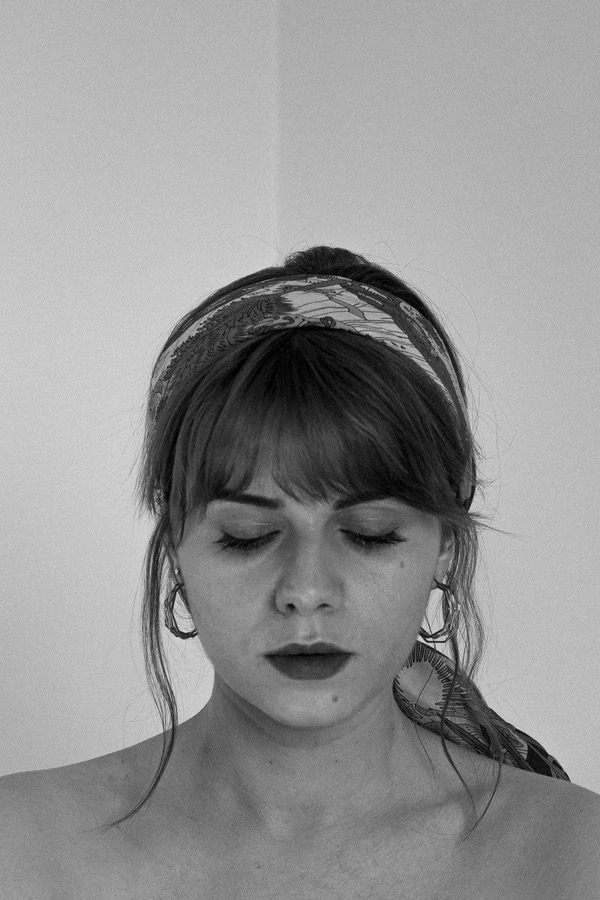 Portret kobiety z zamkniętymi oczami, w chustce na głowie, z kolczykami w uszach, w czerni i bieli.