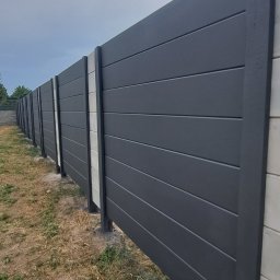 IMPERIUM Firma Handlowo-Usługowa - Nowoczesne ogrodzenie z paneli w kolorze antracytowym, z betonowymi słupkami, widoczne z boku, z suchą trawą u podstawy.