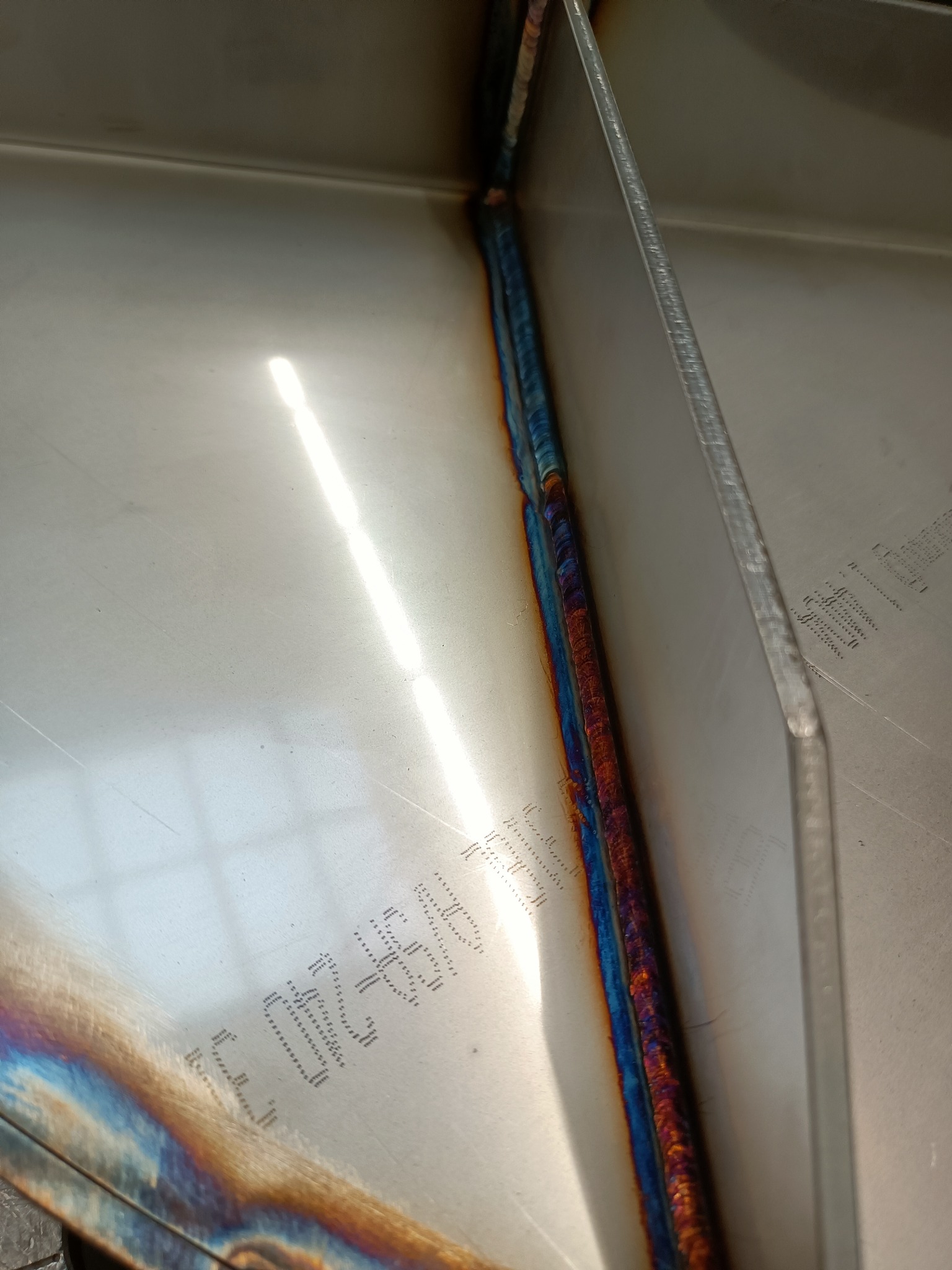 Spoina spawalnicza z charakterystycznymi kolorami utleniania na stali nierdzewnej, widoczne laserowo wycięte napisy na powierzchni metalu