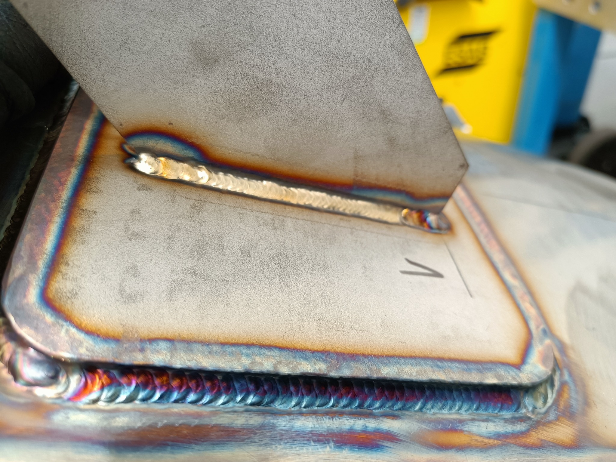 Zbliżenie na spoinę łączącą dwie metalowe płyty, widoczne charakterystyczne przebarwienia termiczne, numer '1' naniesiony obok spoiny.