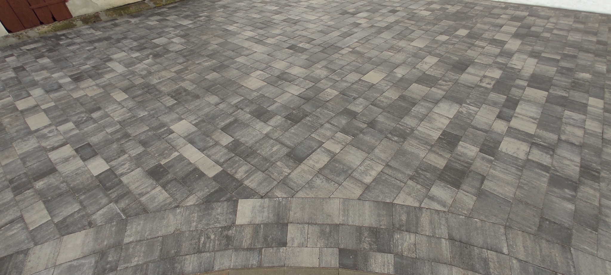 Ułożona szara kostka brukowa w jodełkę, z elementami łuku na obrzeżach.