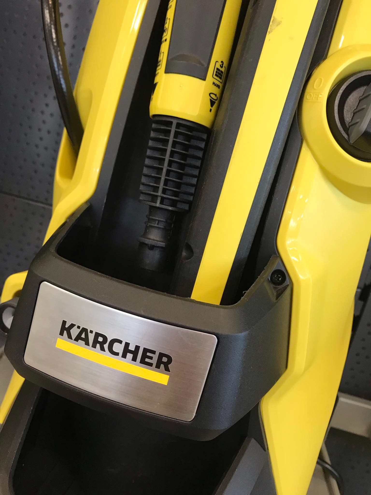 Żółto-czarna myjka ciśnieniowa marki Kärcher, widoczny fragment obudowy, uchwyt z dyszą i logo na srebrnej tabliczce.