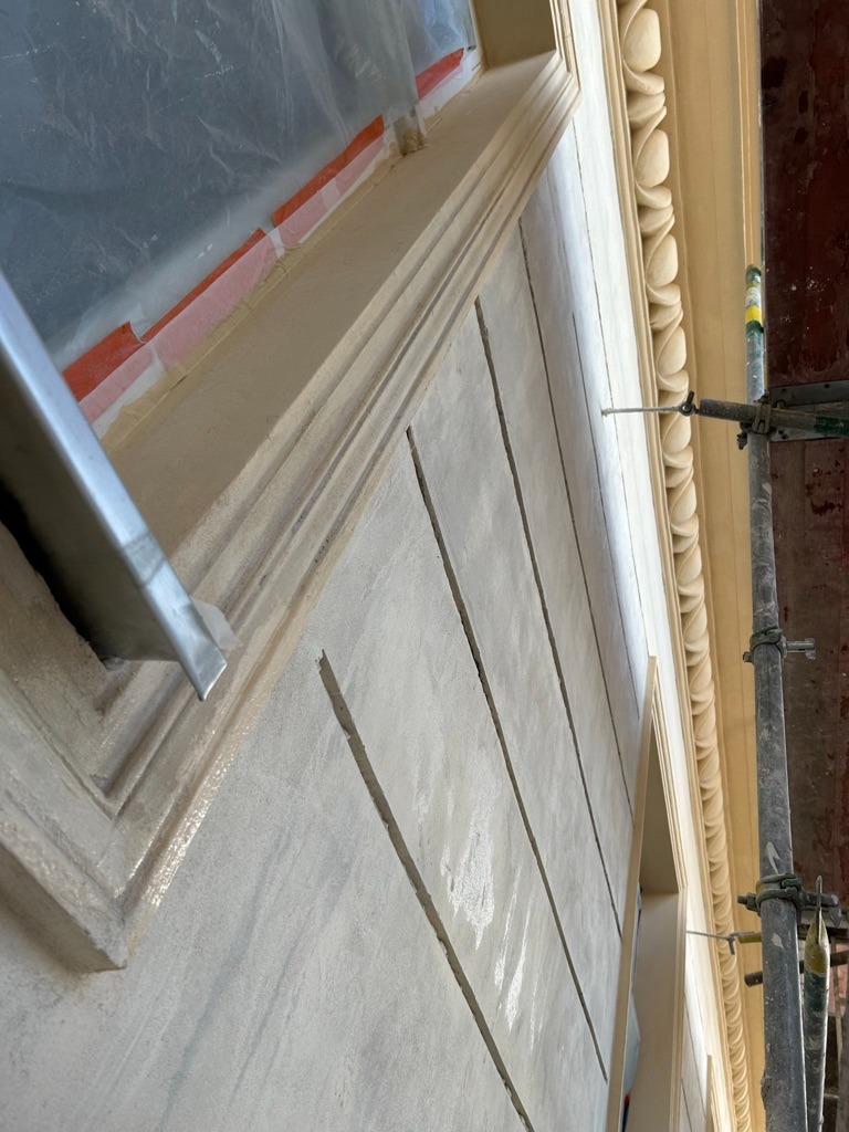 Renowacja elewacji kamienicy z widocznymi detalami architektonicznymi, zabezpieczonym oknem i fragmentem rusztowania.