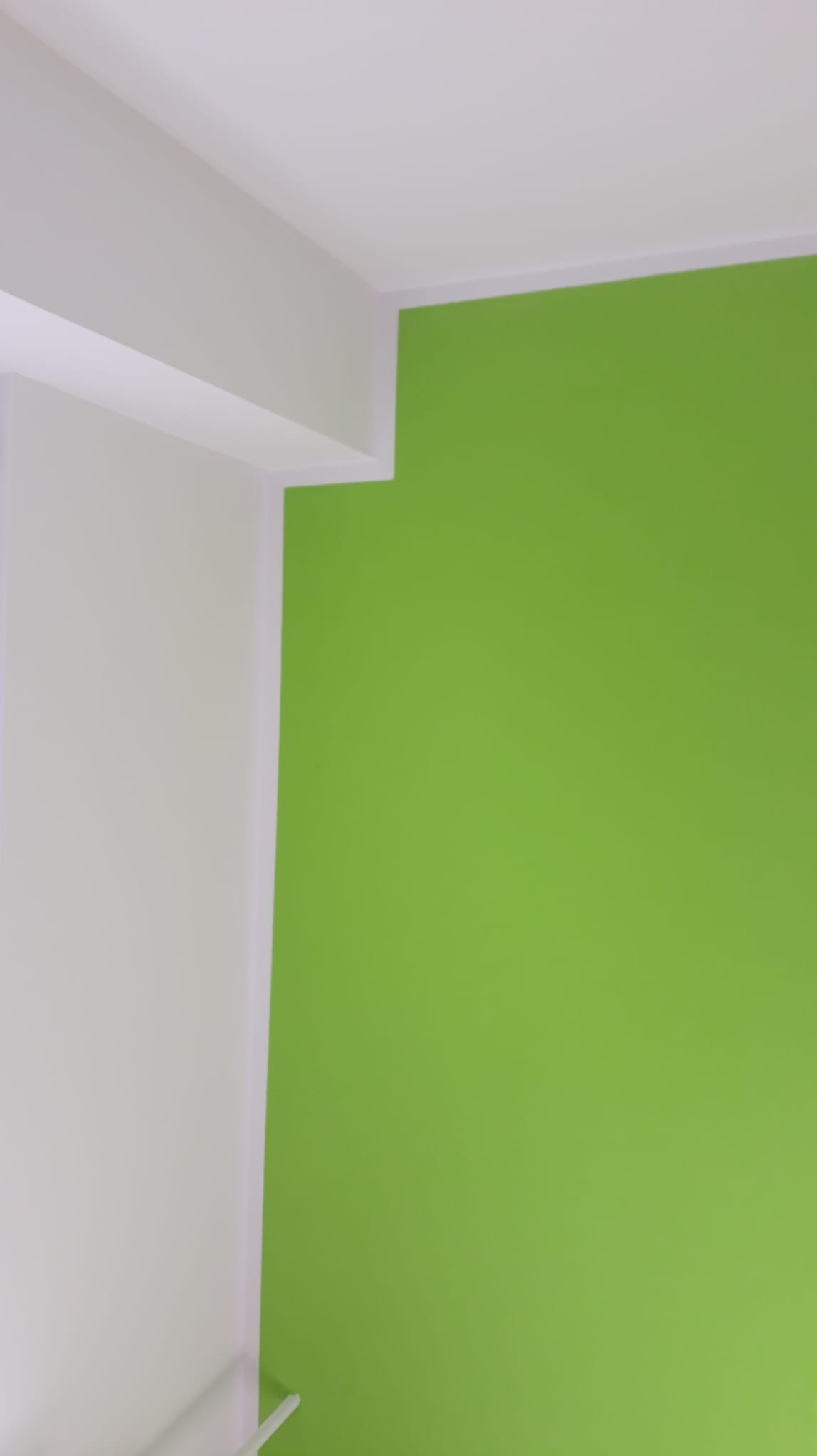 Fragment pomalowanego na zielono narożnika pokoju z białym sufitem i ścianą, widoczny z bliska.