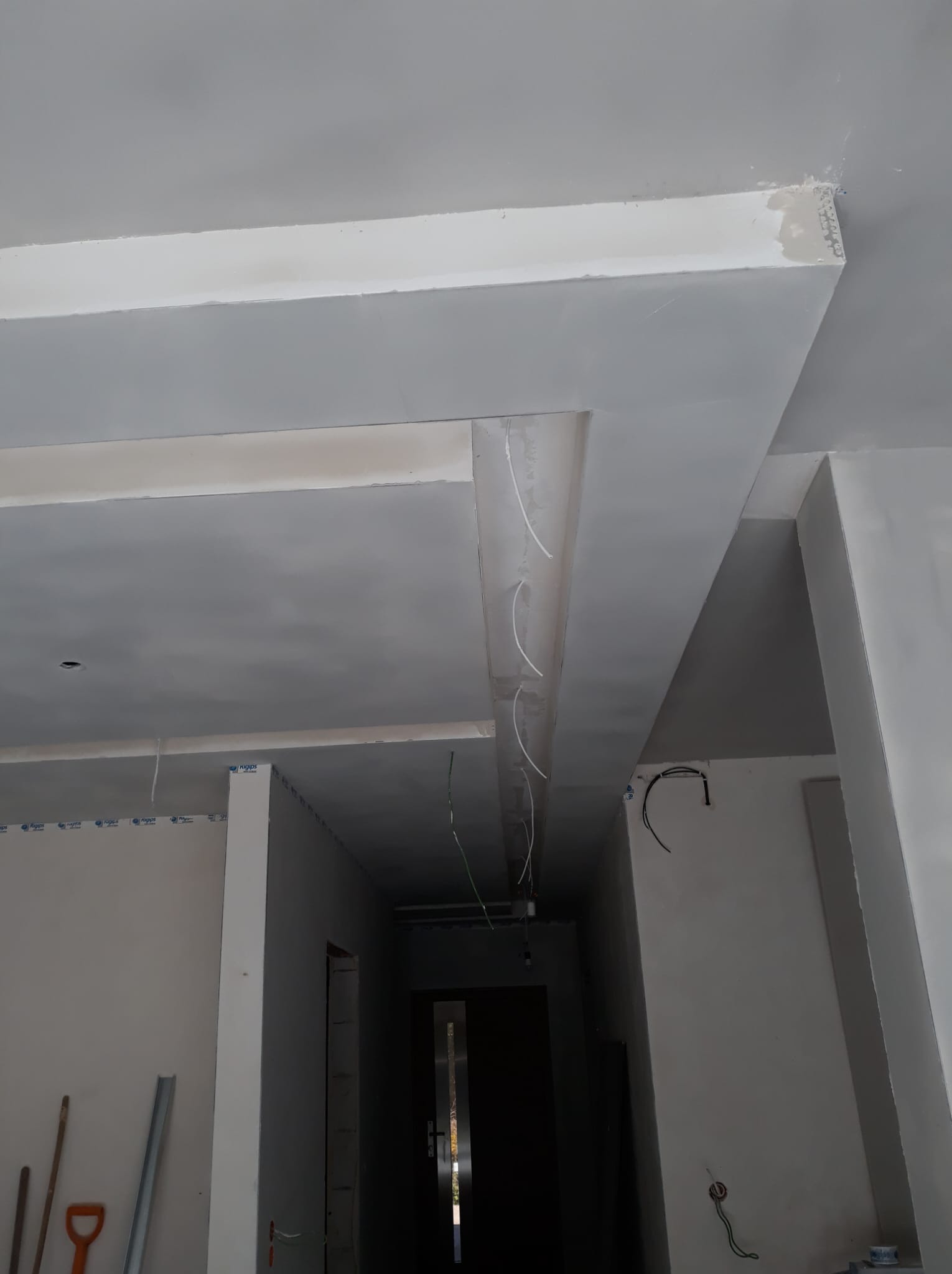 Sufit podwieszany z elementami dekoracyjnymi w trakcie prac, widoczne kable i niedoskonałości w narożnikach, szpachlowane powierzchnie, pomieszczenie w stanie surowym.