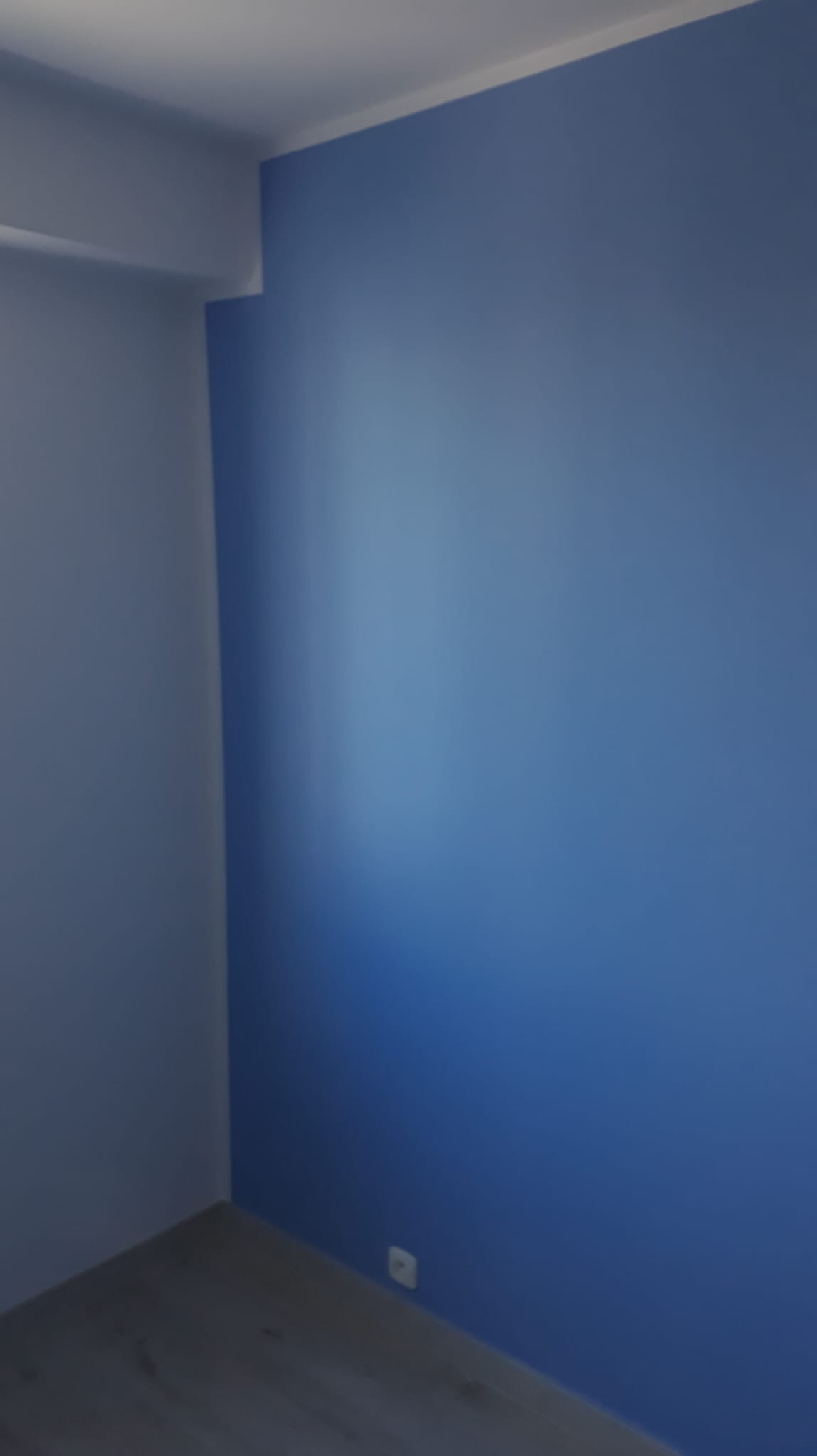 Pomieszczenie po malowaniu ścian na dwa odcienie niebieskiego, widoczny fragment podłogi z panelami i biała listwa sufitowa.