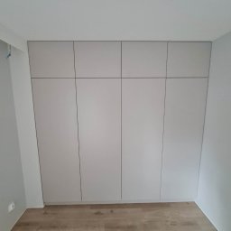 Prima stolarz - Jasnoszara szafa wnękowa z czterema drzwiami, dopasowana do sufitu, z widoczną podłogą z paneli w odcieniach brązu i szarości.