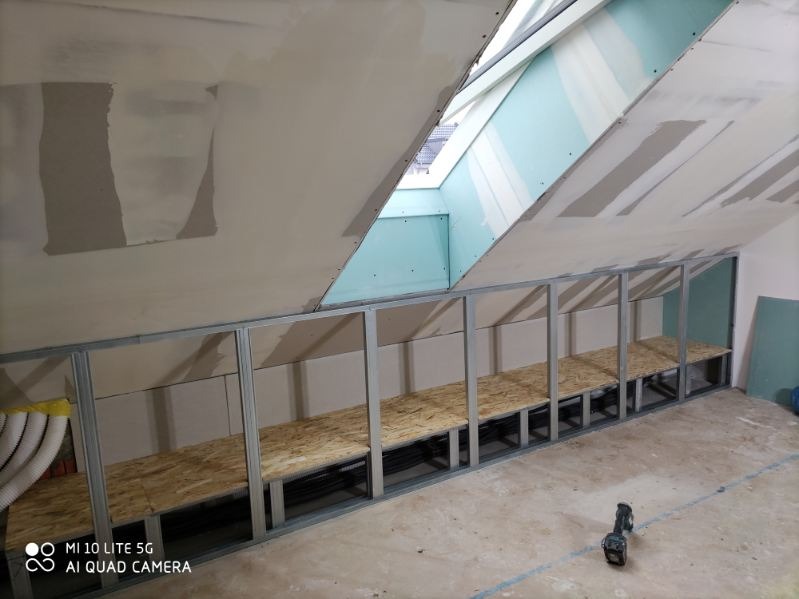 Skośny sufit z oknem połaciowym i metalową konstrukcją w Bielicach Nowych. Widoczne płyty OSB. Prace wykończeniowe na poddaszu.