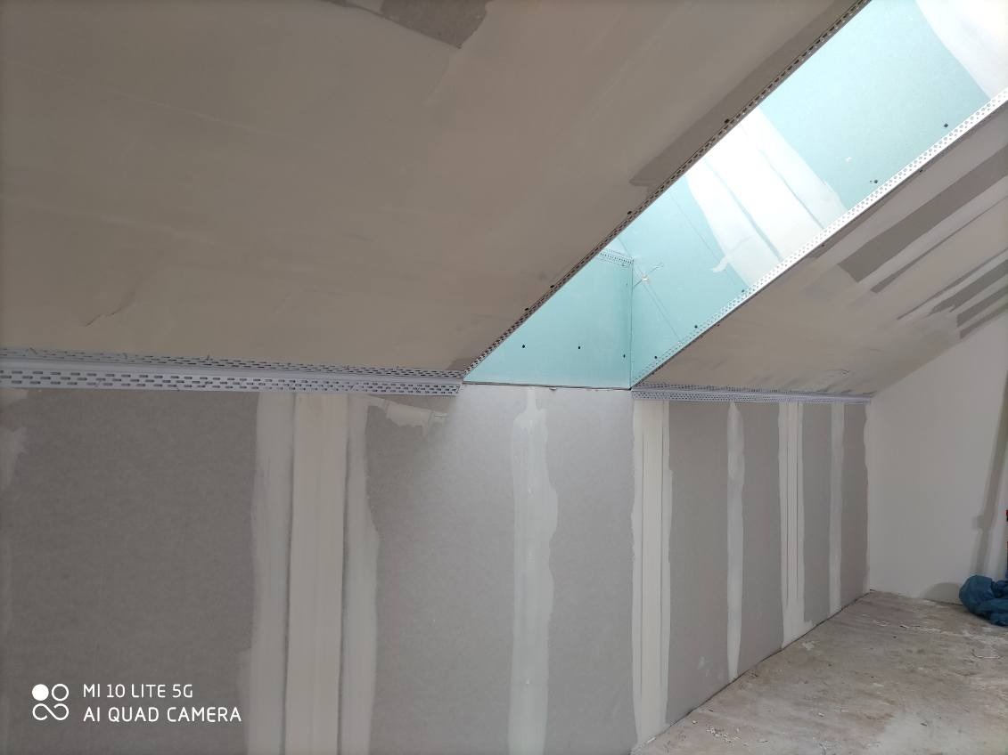 Poddasze w trakcie wykańczania: płyty gipsowe na ścianach i skośnym suficie, widoczne profile i szpachlowane łączenia. Przygotowanie do malowania.