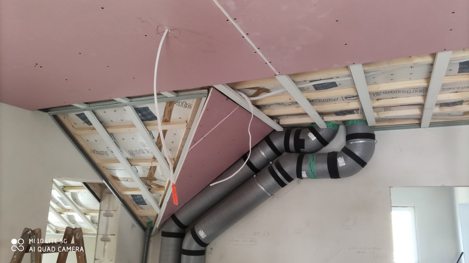 Montaż sufitu podwieszanego z płyt kartonowo-gipsowych na poddaszu, widoczne rury wentylacyjne i konstrukcja metalowa. Prace wykończeniowe w trakcie realizacji.