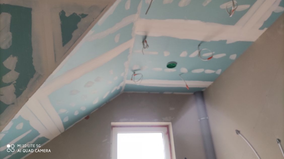 Skośny sufit poddasza z zamontowanymi płytami gipsowo-kartonowymi, widoczne przewody elektryczne i wygładzone łączenia płyt.