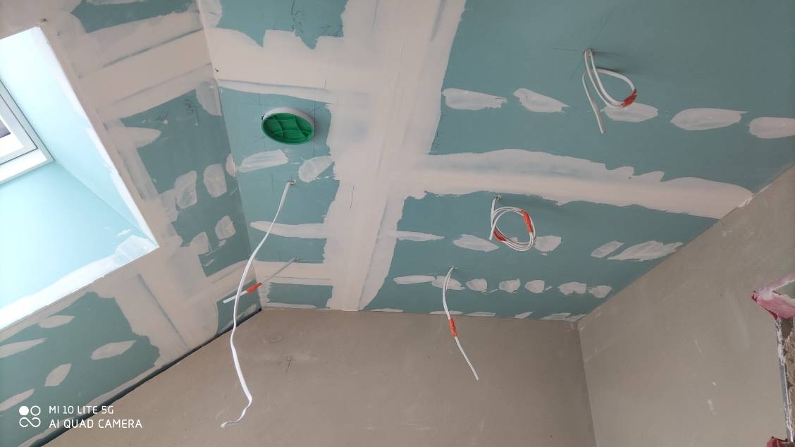 Skośny sufit z płyt kartonowo-gipsowych w trakcie szpachlowania, widoczne kable elektryczne i okno połaciowe. Praca w toku.
