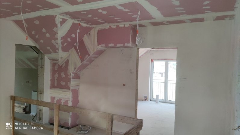 Wnętrze w trakcie prac wykończeniowych: ściany i sufit pokryte płytami gipsowymi, widoczne łączenia i kable. Fragment drewnianej konstrukcji w dolnej części kadru.