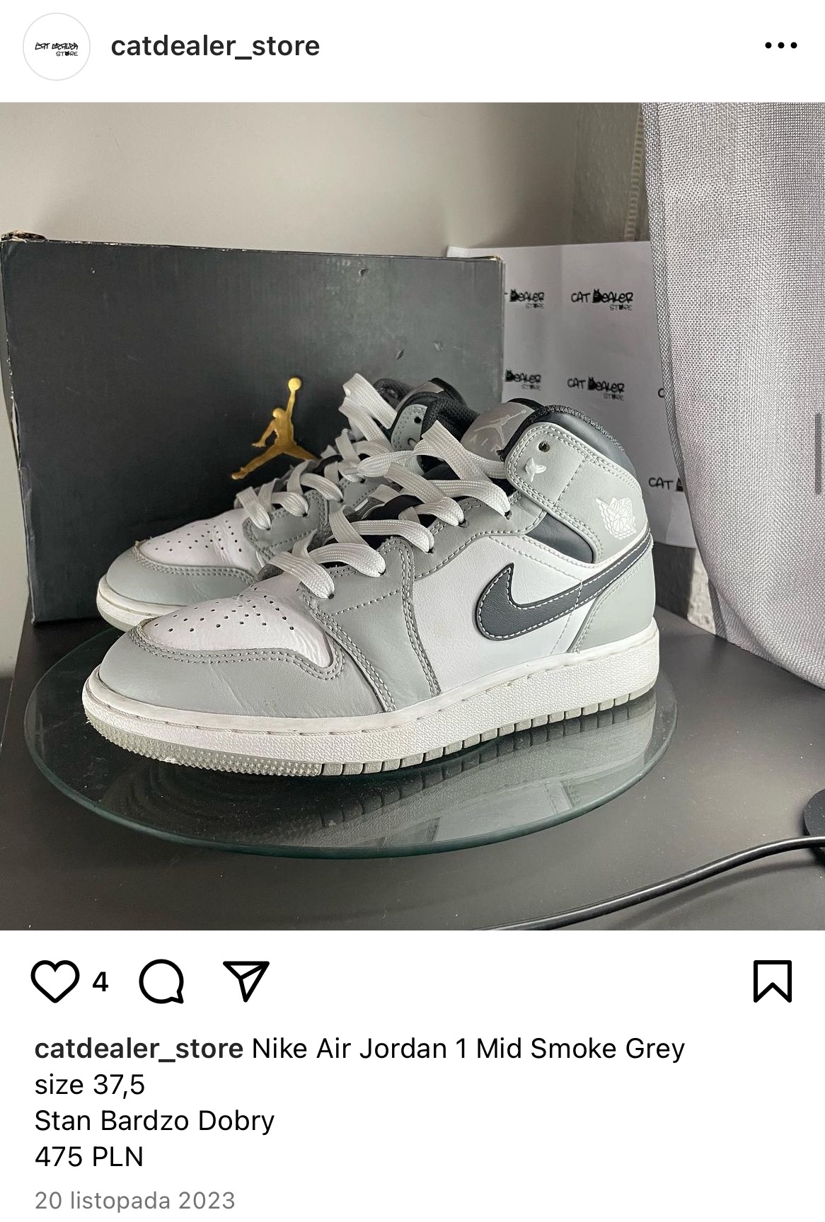 Para szaro-białych sneakersów Nike Air Jordan 1 Mid Smoke Grey, rozmiar 37.5, na szklanej podstawie, z pudełkiem w tle.