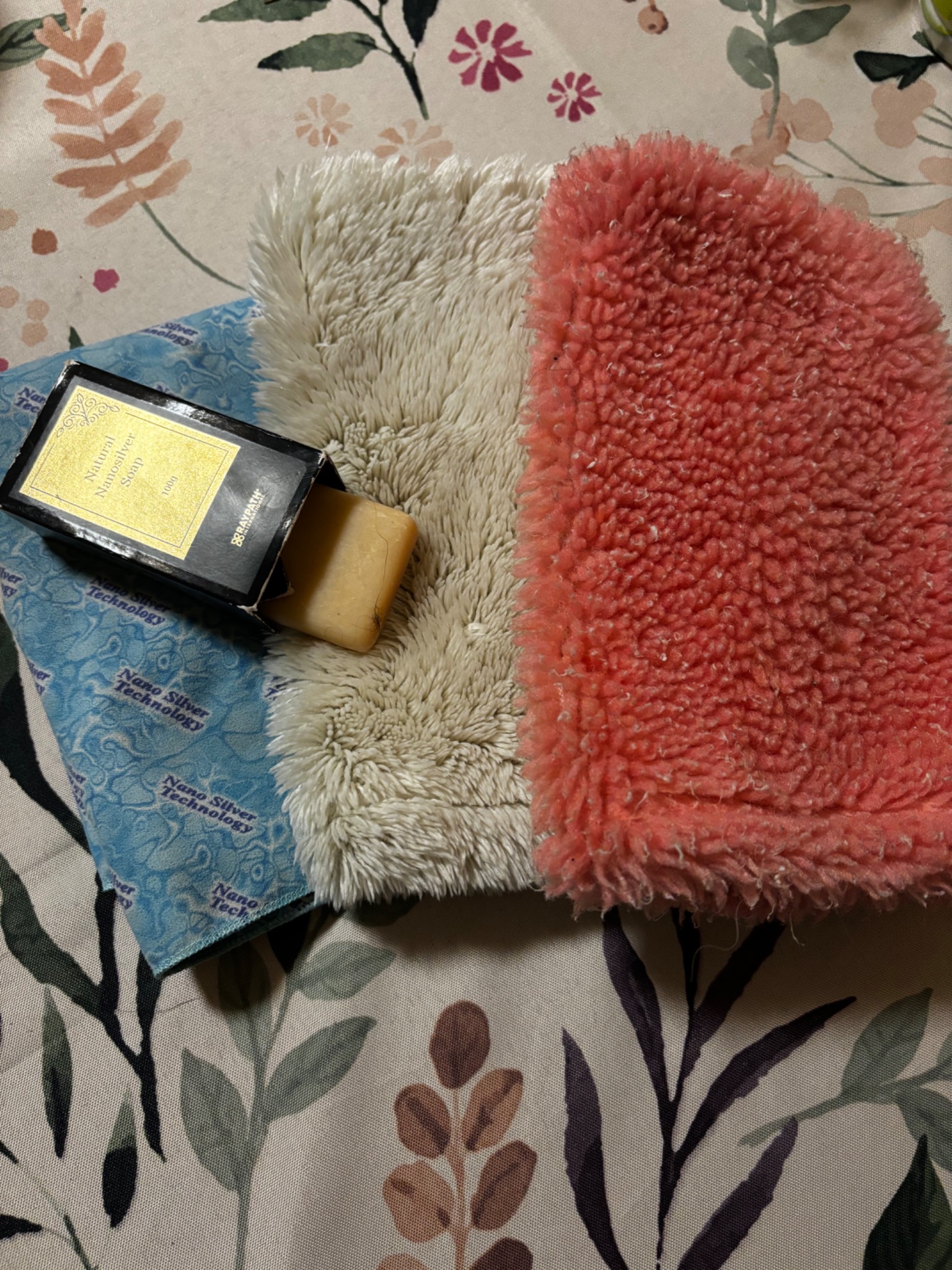Nanosilver soap in open box, next to fluffy cleaning mitts in beige and coral, on a floral patterned surface.