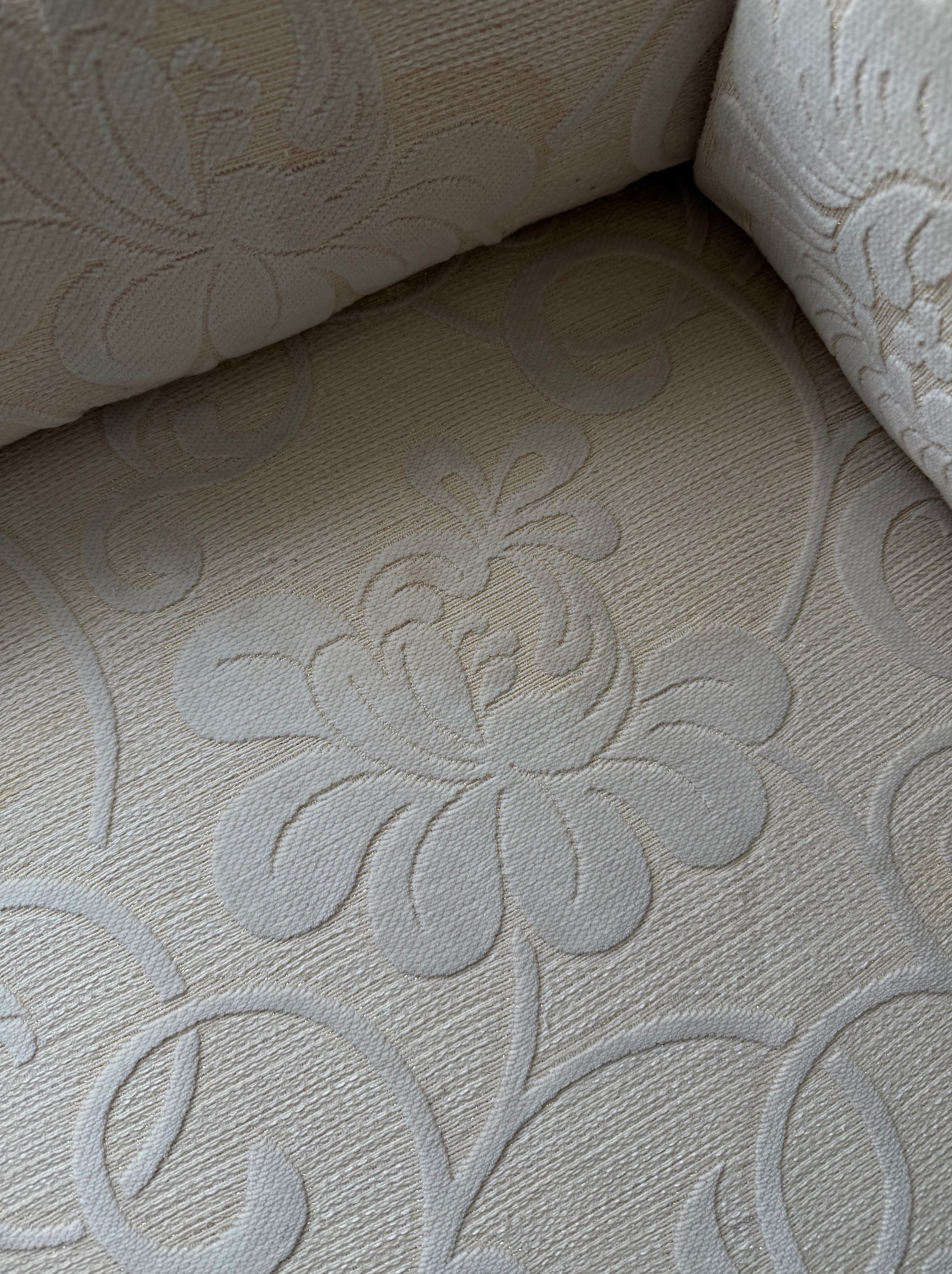 Kremowa tapicerka sofy z wytłaczanym, kwiatowym wzorem, widoczna z bliska. Delikatna tekstura materiału i subtelne światłocienie podkreślają elegancję.