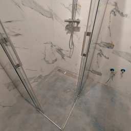 IMD-BUD - Kabina prysznicowa walk-in z marmurowymi płytkami na ścianach i szarym, betonowym wykończeniem podłogi. Widoczne chromowane elementy armatury i odpływ liniowy w posadzce.