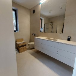 IMD-BUD - Nowoczesna łazienka z beżowymi płytkami, wiszącą toaletą i szafką pod umywalkę z szufladami, widoczne pudełka po ceramice przed montażem.