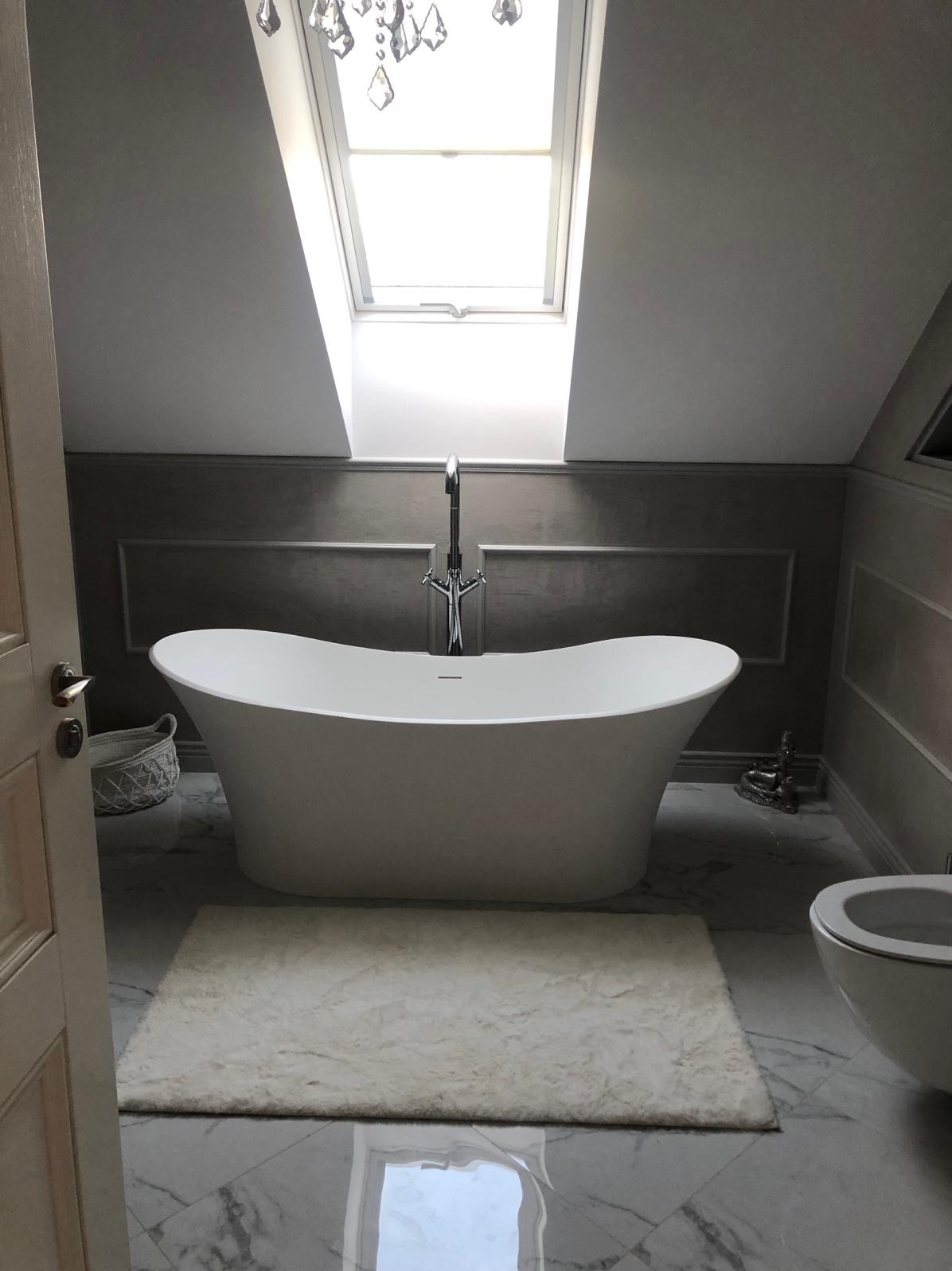 Wolnostojąca wanna w nowoczesnej łazience z marmurową podłogą, oknem dachowym i dekoracyjną armaturą.
