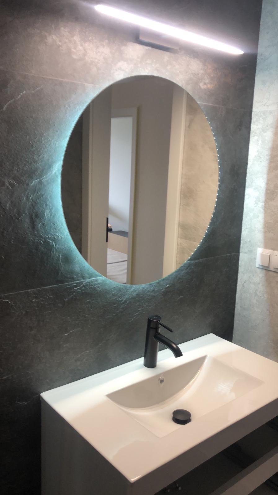 Nowoczesna łazienka z okrągłym lustrem podświetlanym LED, czarną armaturą i szarą płytką imitującą kamień.