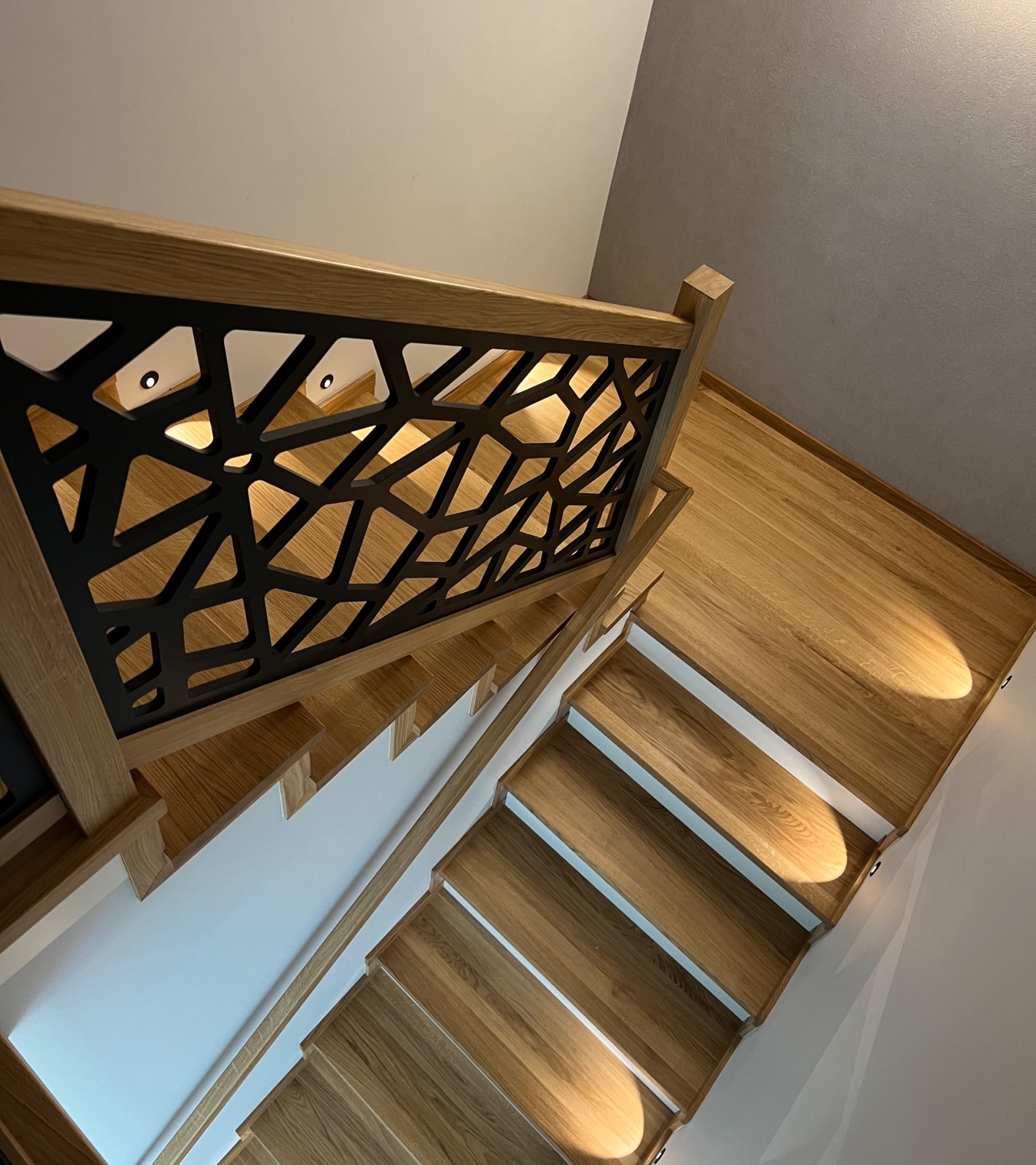 Nowoczesne schody z drewna dębowego z ażurową balustradą w kolorze czarnym i podświetleniem LED stopni, widok z góry.