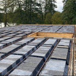 Ihor Kadynskyi - Wznoszenie stropu Teriva z pustaków szalunkowych na tle zieleni i jeziora, widoczny szalunek otworu w stropie.