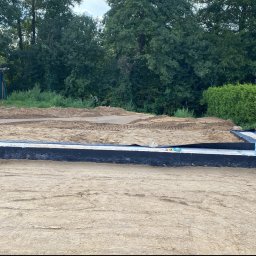 Ihor Kadynskyi - Przygotowany teren pod budowę domu z widocznymi fundamentami zabezpieczonymi czarną folią izolacyjną, dwie butelki wody stojące na fundamencie, w tle ziemia wyrównana pod wylewkę i prowizoryczna...