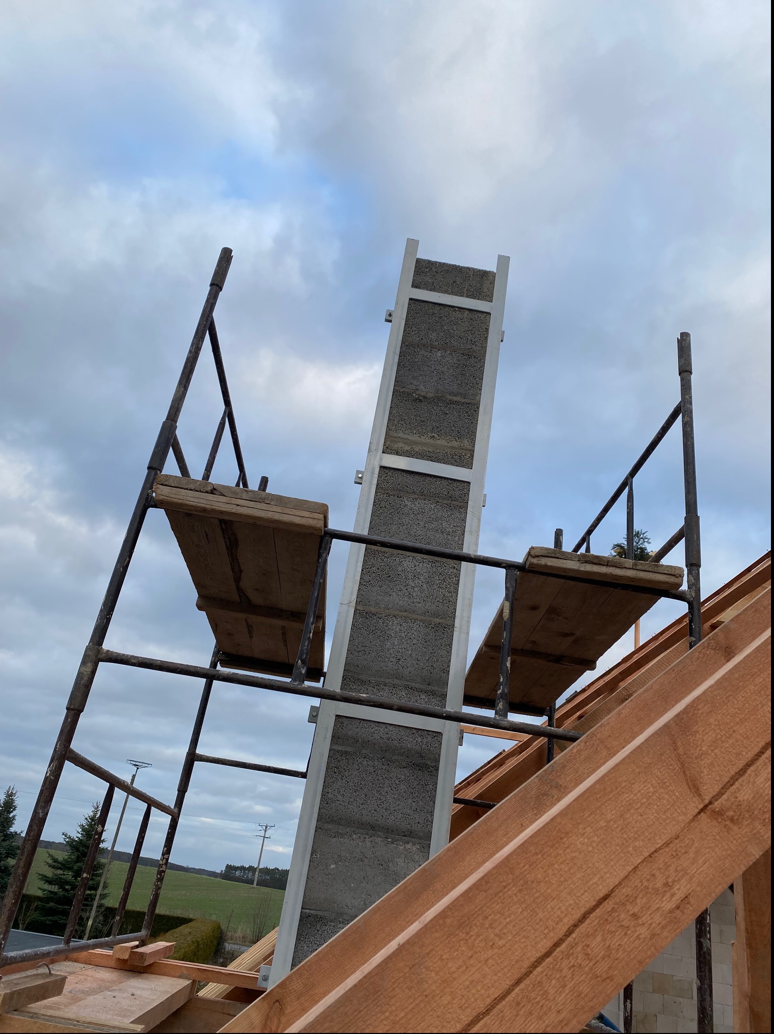 Budowa domu w Świebodzinie: widok na wznoszone ściany z betonu komórkowego, rusztowanie i konstrukcję dachu w trakcie montażu, pochmurne niebo w tle.