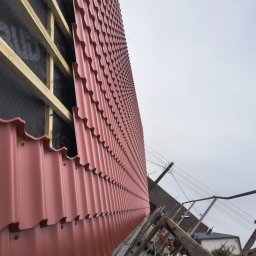 OKTAWIAN LESZCZYK - Montaż blachodachówki w kolorze ceglastym na konstrukcji drewnianej z widoczną membraną dachową, ujęcie z rusztowania.