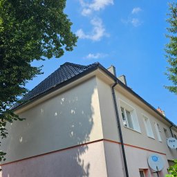 OKTAWIAN LESZCZYK - Dwukondygnacyjny dom z nowym, czarnym dachem z dachówki, beżową elewacją i antenami satelitarnymi na tle błękitnego nieba i zieleni drzew.