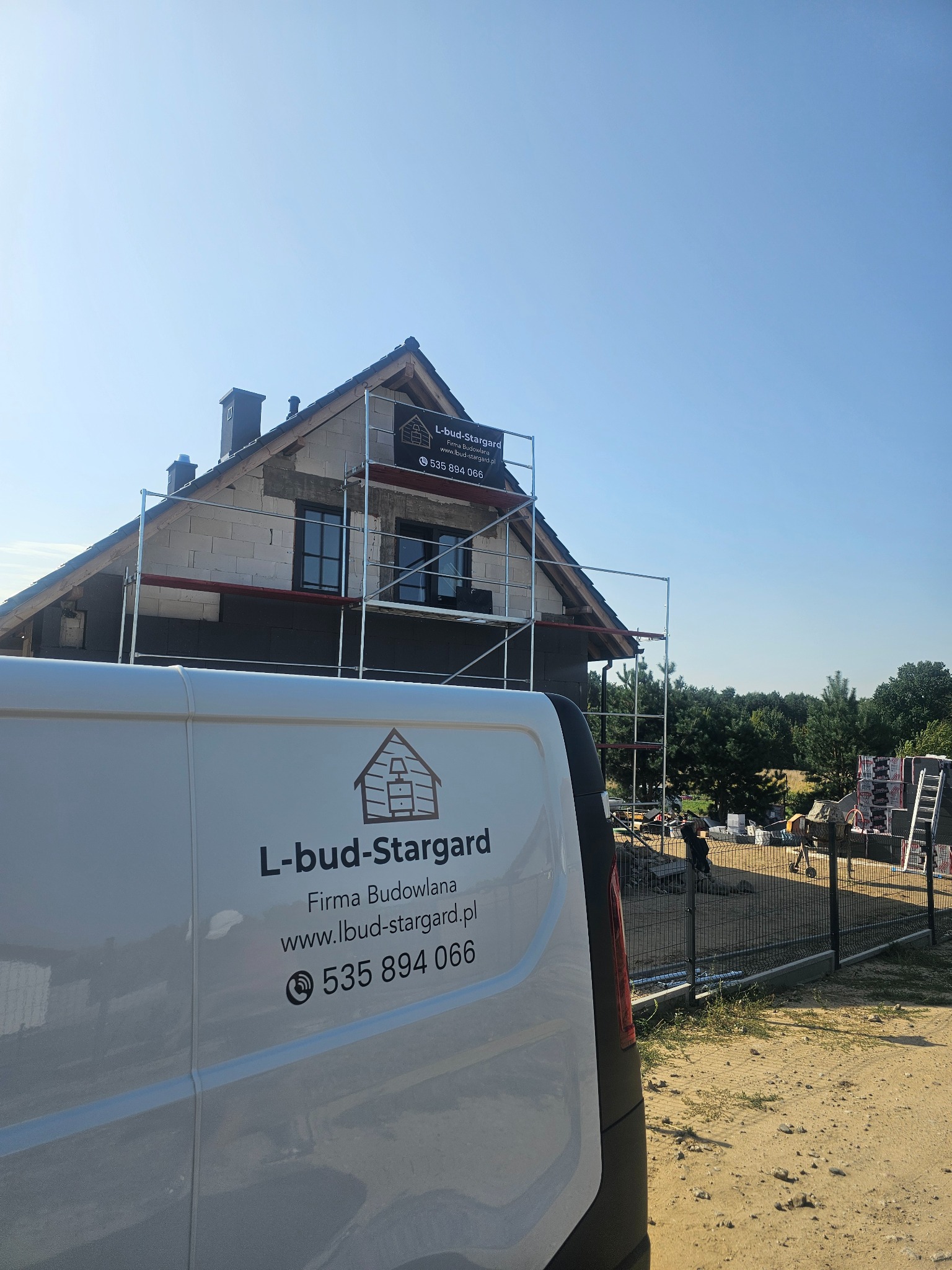 Dom w trakcie prac elewacyjnych z widocznymi rusztowaniami i częściowo ocieploną ścianą, na pierwszym planie samochód dostawczy firmy budowlanej L-bud-Stargard z numerem telefonu.