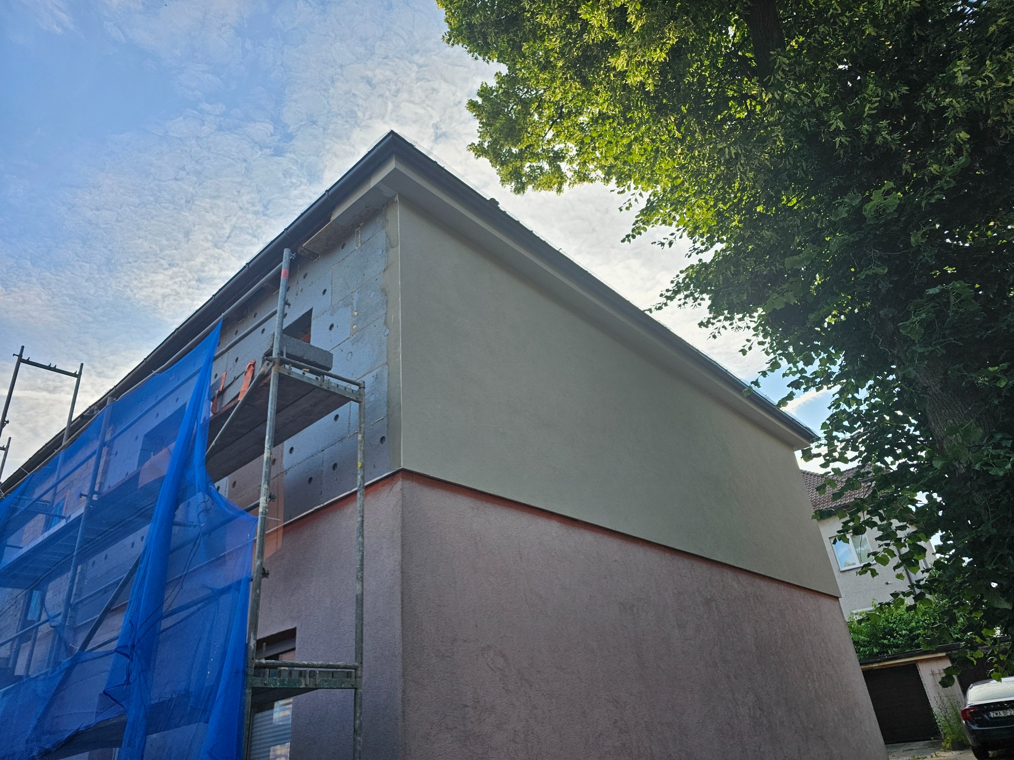 Dwukolorowa elewacja budynku w trakcie prac, z widocznym ociepleniem i rusztowaniem pod błękitnym niebem.