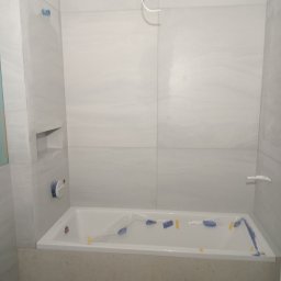 RomBud - Wanna zabezpieczona folią i taśmą malarską podczas prac wykończeniowych w łazience, widoczne jasne płytki na ścianach z wnęką.