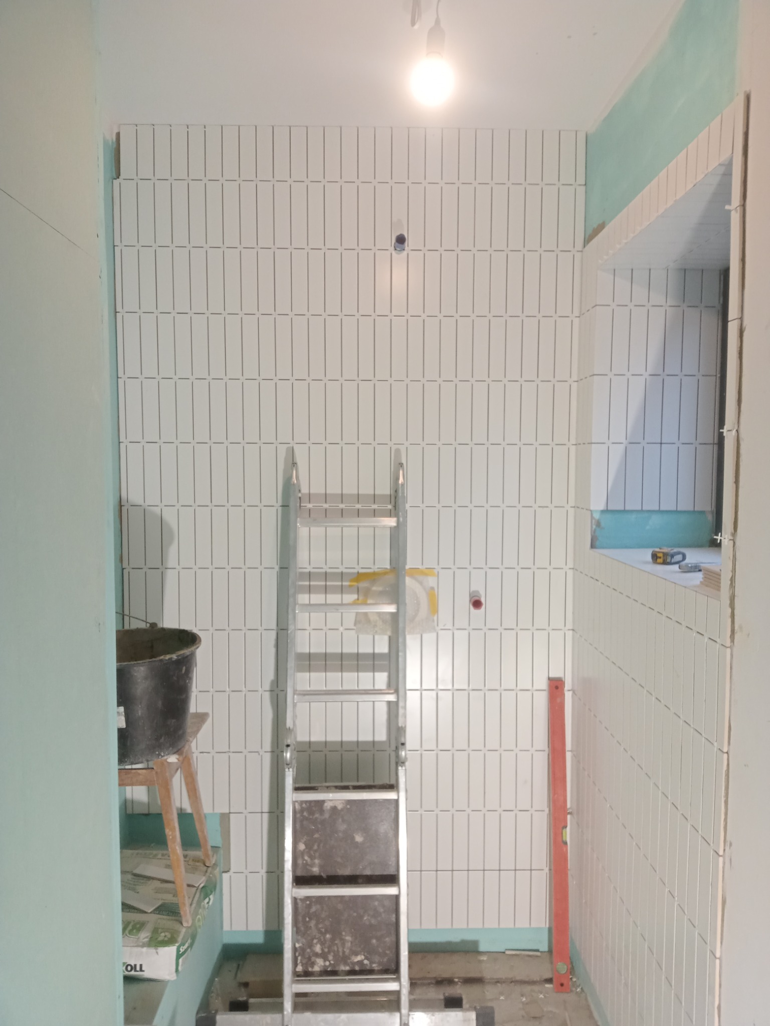 Łazienka w trakcie układania białych, wąskich płytek w pionowym układzie, widoczna drabina malarska i narzędzia, Poznań.