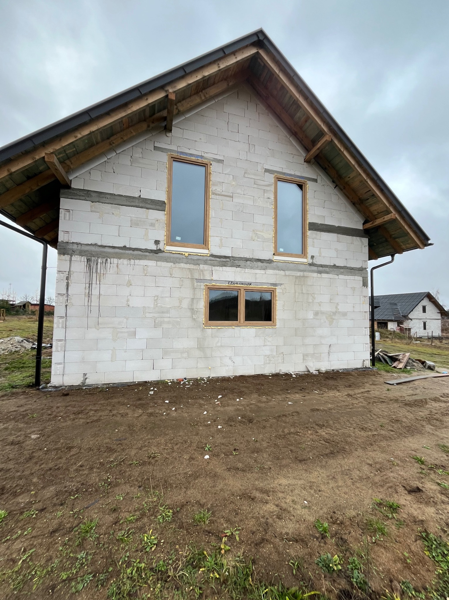 Surowy stan budynku w Kościerzynie z widocznymi oknami z brązowymi ramami, ściany z białych bloczków, przygotowany do dalszych prac wykończeniowych elewacji.