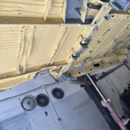 Spód samochodu na podnośniku warsztatowym, pokryty żółtą warstwą ochronną, widoczne elementy konstrukcyjne i zabezpieczone profile.