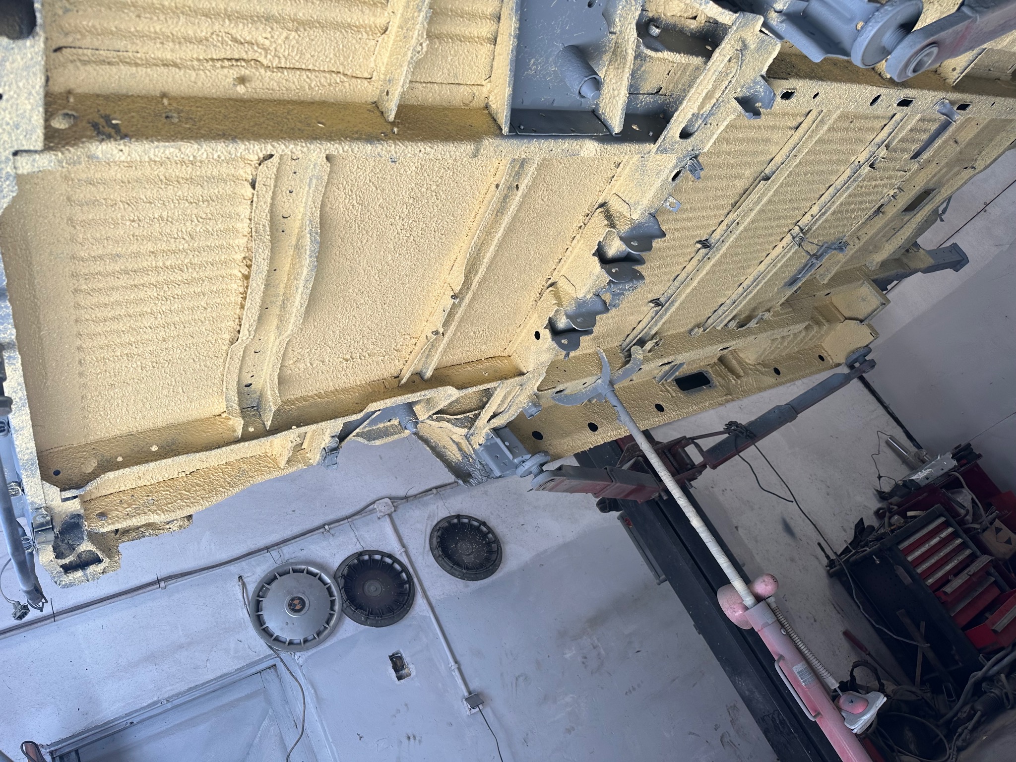 Spód samochodu na podnośniku warsztatowym, pokryty żółtą warstwą ochronną, widoczne elementy konstrukcyjne i zabezpieczone profile.