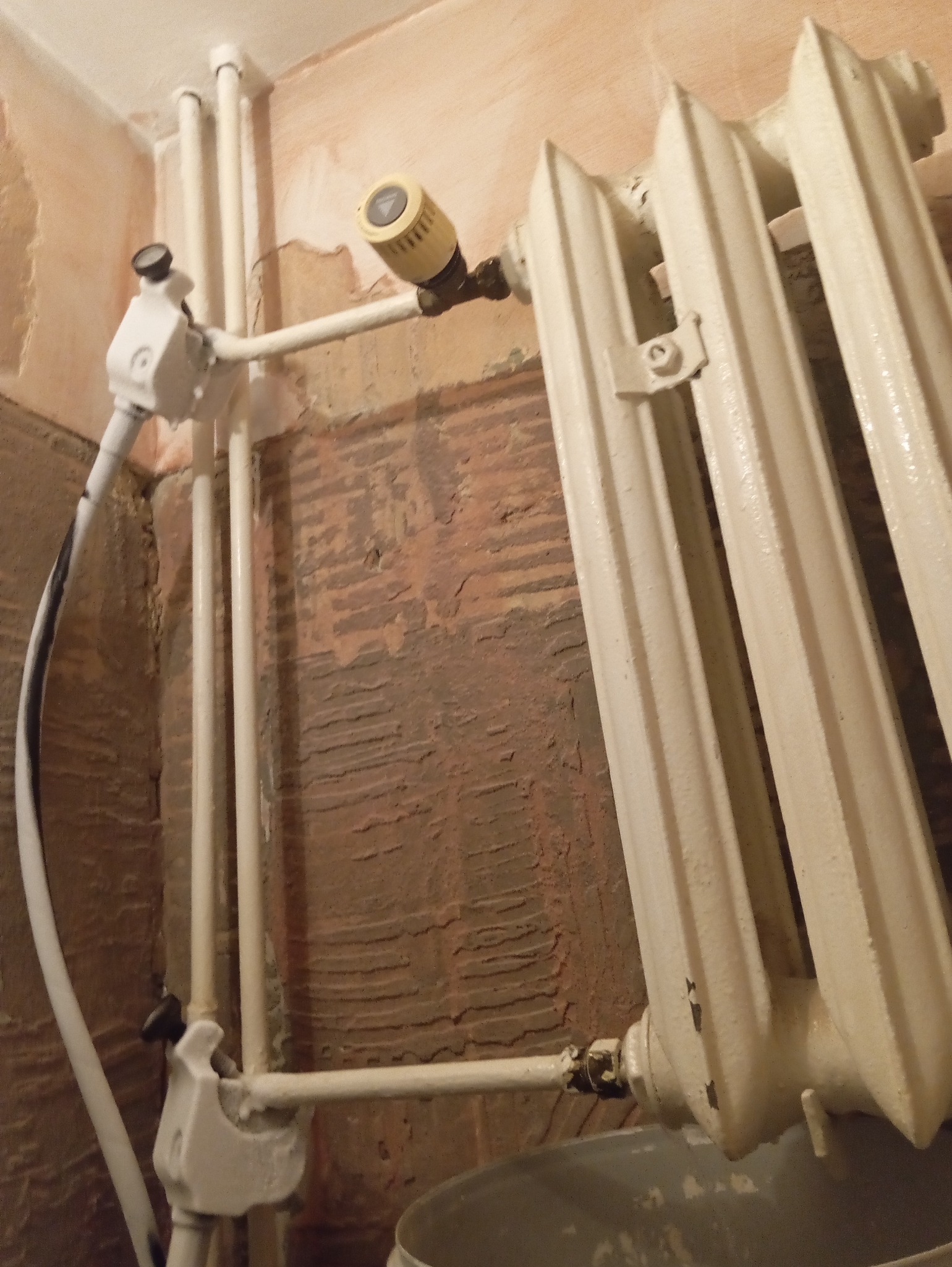 Biały, żeliwny grzejnik żeberkowy z termostatem i nową instalacją rur w surowym wnętrzu podczas remontu.
