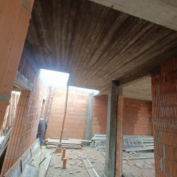 RAF usługi budowlane - Wnętrze surowego domu z cegły ceramicznej, widoczne betonowe stropy i filary. Na podłodze resztki materiałów budowlanych, w tle widoczna osoba.