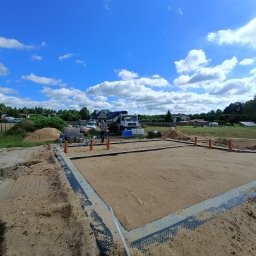 RAF usługi budowlane - Przygotowany teren pod fundamenty domu jednorodzinnego. Widoczny obrys ław fundamentowych, piasek zasypowy, betonowy wieniec i pracownik nadzorujący prace.