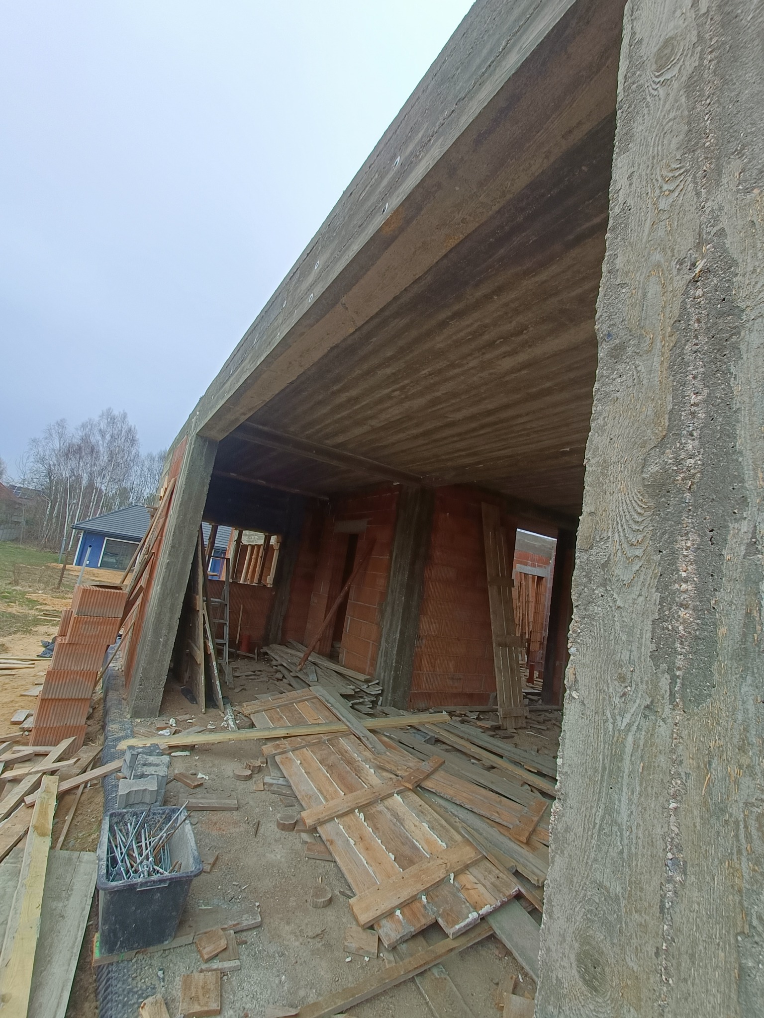Surowy stan budowy domu z cegły: widoczne ściany, betonowy strop i przygotowane deski. Kąt ujęcia z dołu podkreśla strukturę betonu i etap prac murarskich.