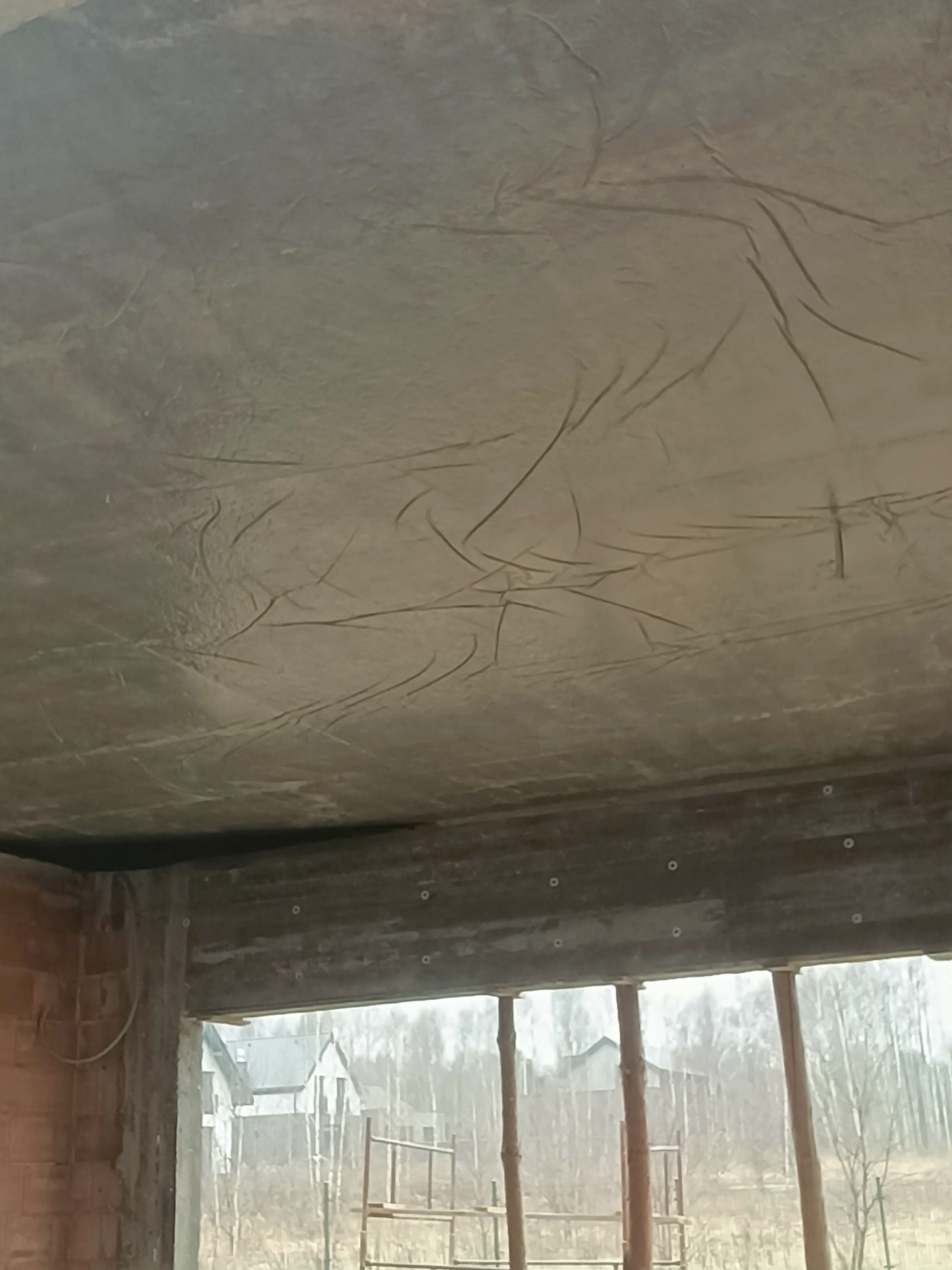 Wykończony strop dwupoziomowy z widoczną fakturą betonu, surowy stan, widok z wnętrza budynku na zewnątrz, w tle zieleń i budynki.