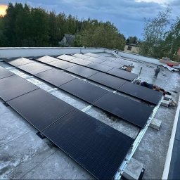 SMART PV ALEKSANDRA JABŁOŃSKA - Montaż paneli fotowoltaicznych na płaskim dachu, widoczni dwaj pracownicy w trakcie instalacji, żółty samochód dostawczy zaparkowany w tle.