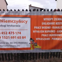 Baner reklamowy firmy R&H Niemczyńscy oferującej usługi brukarskie, wywieszony na płocie, z numerami telefonów i adresem e-mail, ilustrowany kreskówkowymi postaciami przy pracy.