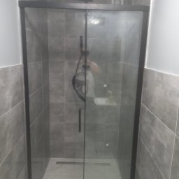 Aa bud - Nowoczesna kabina prysznicowa z przesuwanymi drzwiami w czarnej ramie, szare płytki na ścianach, biała marmurowa podłoga z odpływem liniowym.