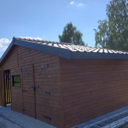 Aa bud - Drewniana altana z ciemnobrązowymi deskami i szarą dachówką, z drabiny opartą o bok, na tle błękitnego nieba i zieleni drzew.