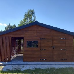 Aa bud - Drewniana konstrukcja z zadaszeniem, częściowo osłonięta pionowymi listwami, z drabiną wewnątrz, na tle zieleni i błękitnego nieba.